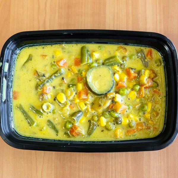 Overhead view of a black container filled with yellow vegetable curry on a wooden table.