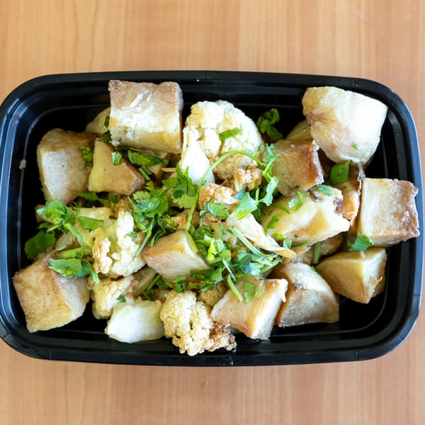 Top-down view of a black takeout container filled with fried taro, cauliflower, and cilantro.