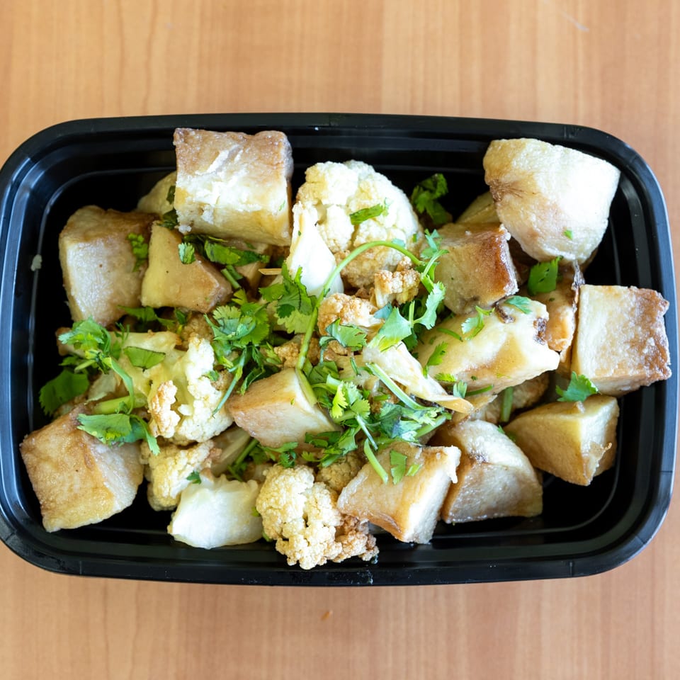 Top-down view of a black takeout container filled with fried taro, cauliflower, and cilantro.