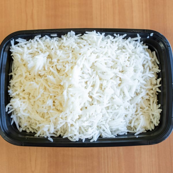 Fluffy white basmati rice in a black rectangular takeout container on a wooden table.