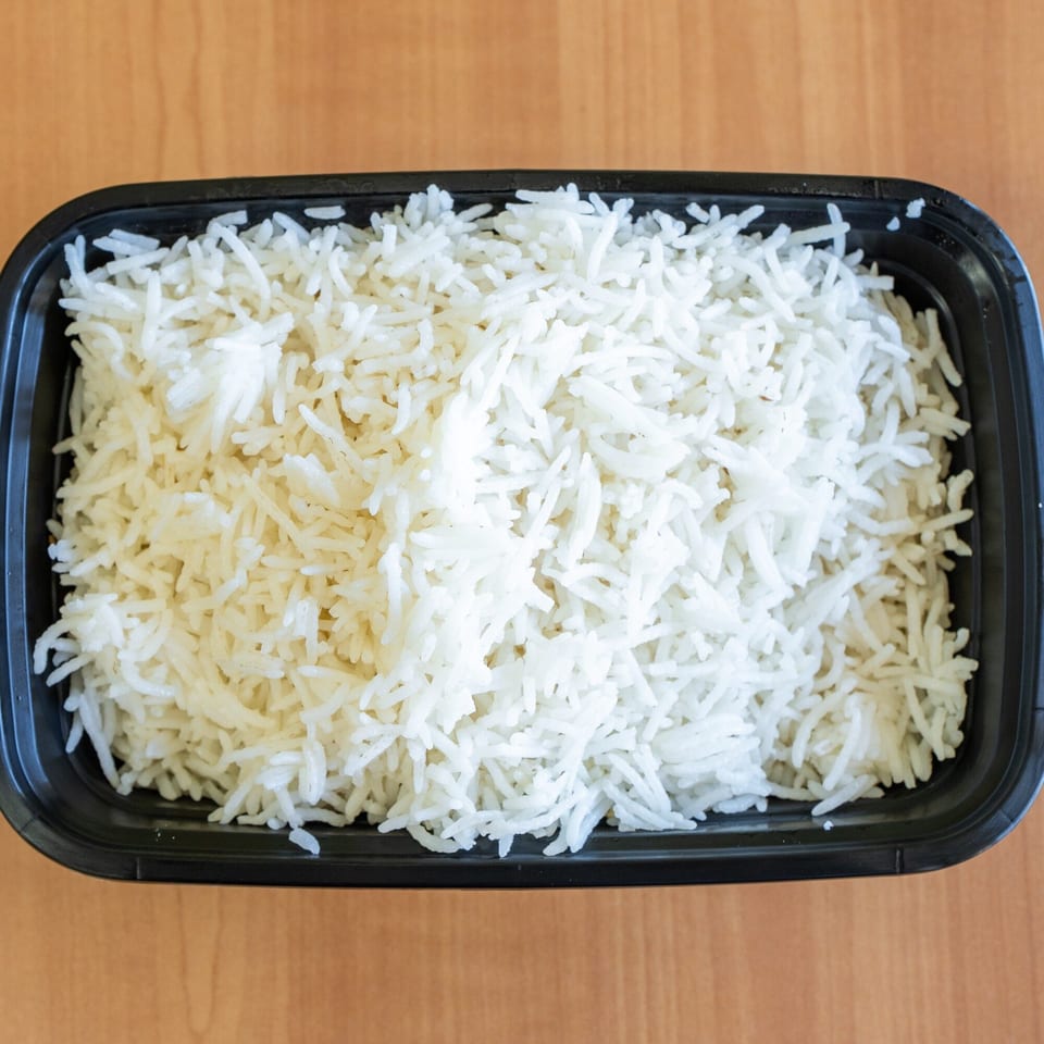 Fluffy white basmati rice in a black rectangular takeout container on a wooden table.