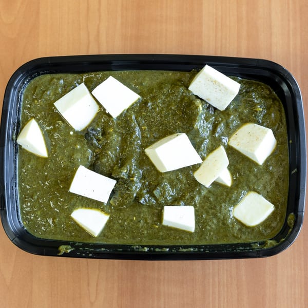 Overhead view of saag paneer, a green spinach dish with white cheese cubes, in a black container.