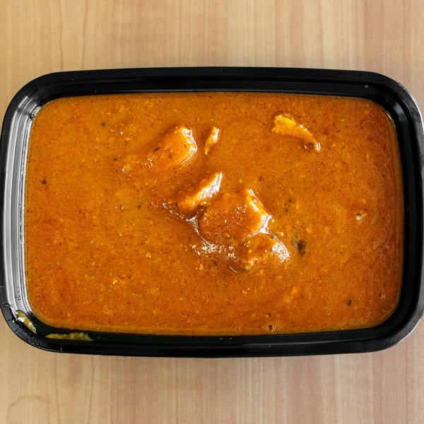 Overhead view of a black takeout container filled with orange-red curry and chicken pieces.