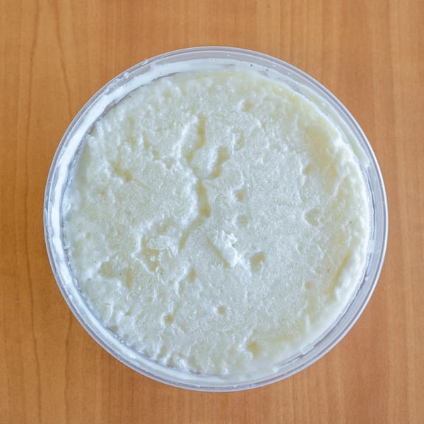 Overhead view of a clear plastic container filled with white, creamy rice pudding on a wooden table.