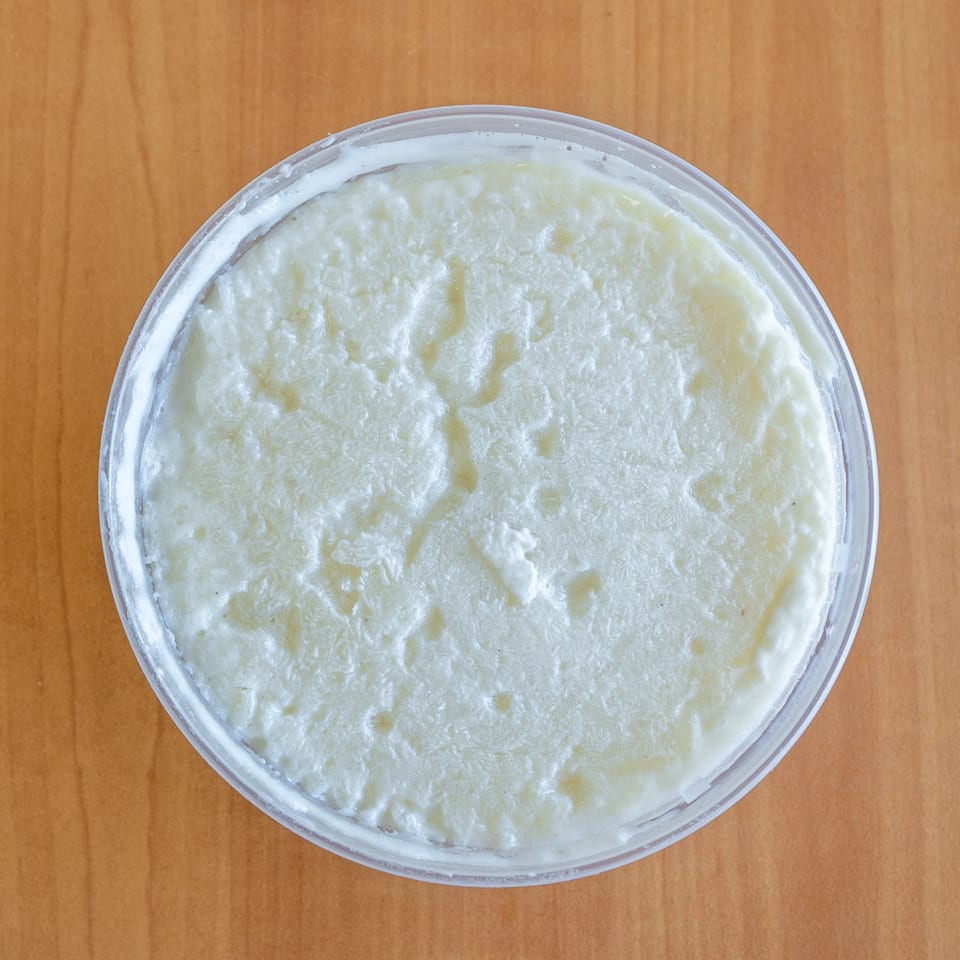 Overhead view of a clear plastic container filled with white, creamy rice pudding on a wooden table.