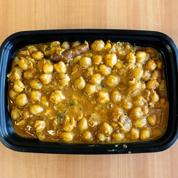 Chana masala, a chickpea curry, in a black takeout container on a wooden table.