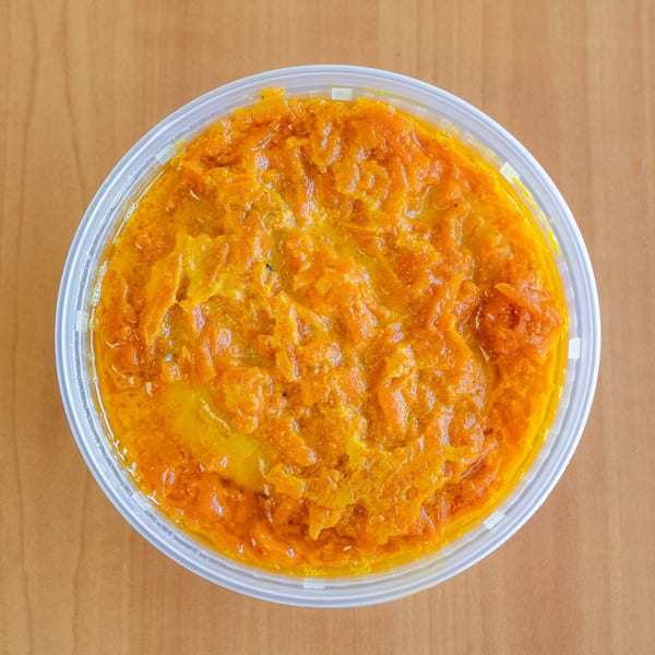 Overhead view of a clear plastic container filled with bright orange, chunky gajar halwa.